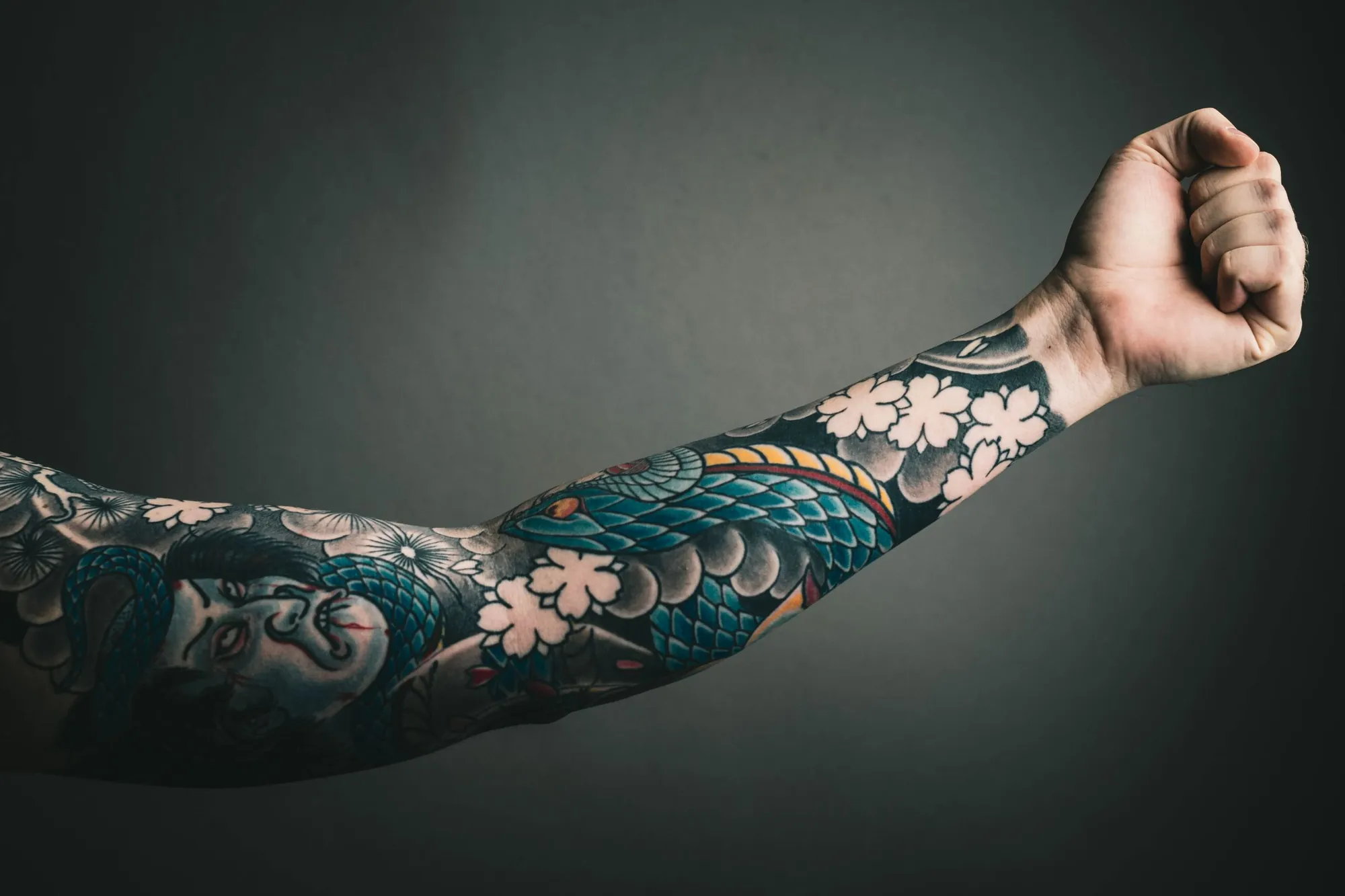 Braț tatuat complet în stil japonez, cu flori de cireș roz și valuri